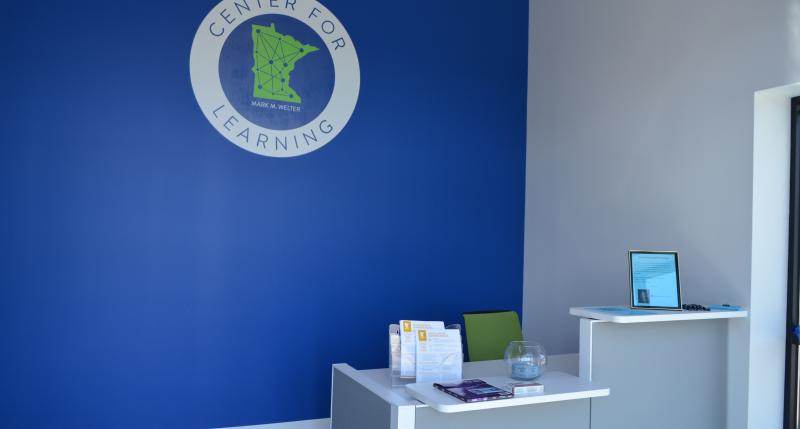 Front desk against navy blue wall with 2x2 foot wide and tall Center for Learning logo featured in the center of the wall