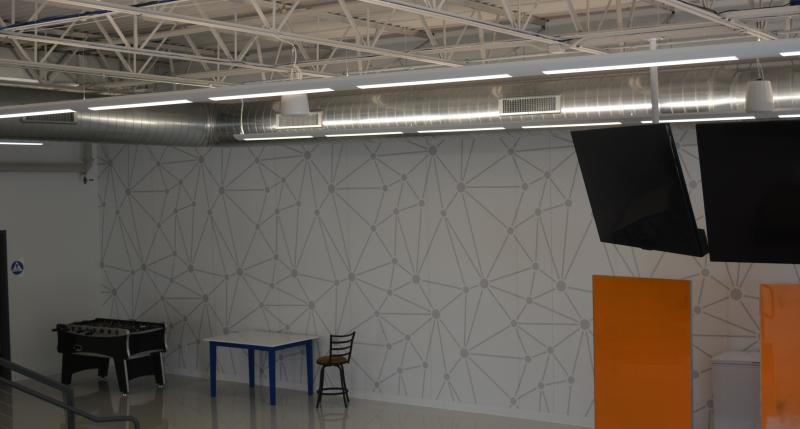 White wall with grey webbed mural in the Center for Learning space. There are two small TVs mounted from the ceiling and two orange white boards around 6 feet tall and 3 feet wide.