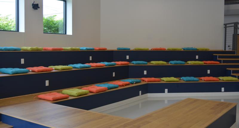 3 level riser seating with square orange, green, and blue colored seat cushions sporadically placed across the risers