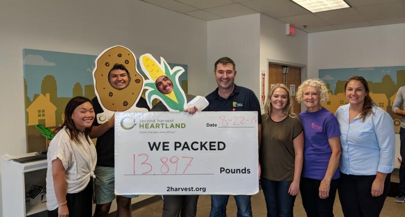 May Yang, Frankie Becerra, Dillon Forcier, Mike Dean, Courtney Brockman, Joyce Petsch, Lindsay Barton holding pounds packed sign at Second Harvest Heartland in August 2018.