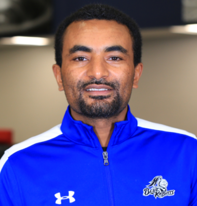 Dame Gamada, is a black man with a short beard and short, curly black hair. He is wearing a royal blue Under Armor zip up and is smiling at the camera. This photo is courtesy of DCTC