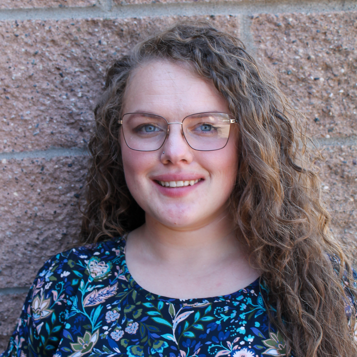 headshot of danielle miller, advocacy storytelling associate against red/copper brick