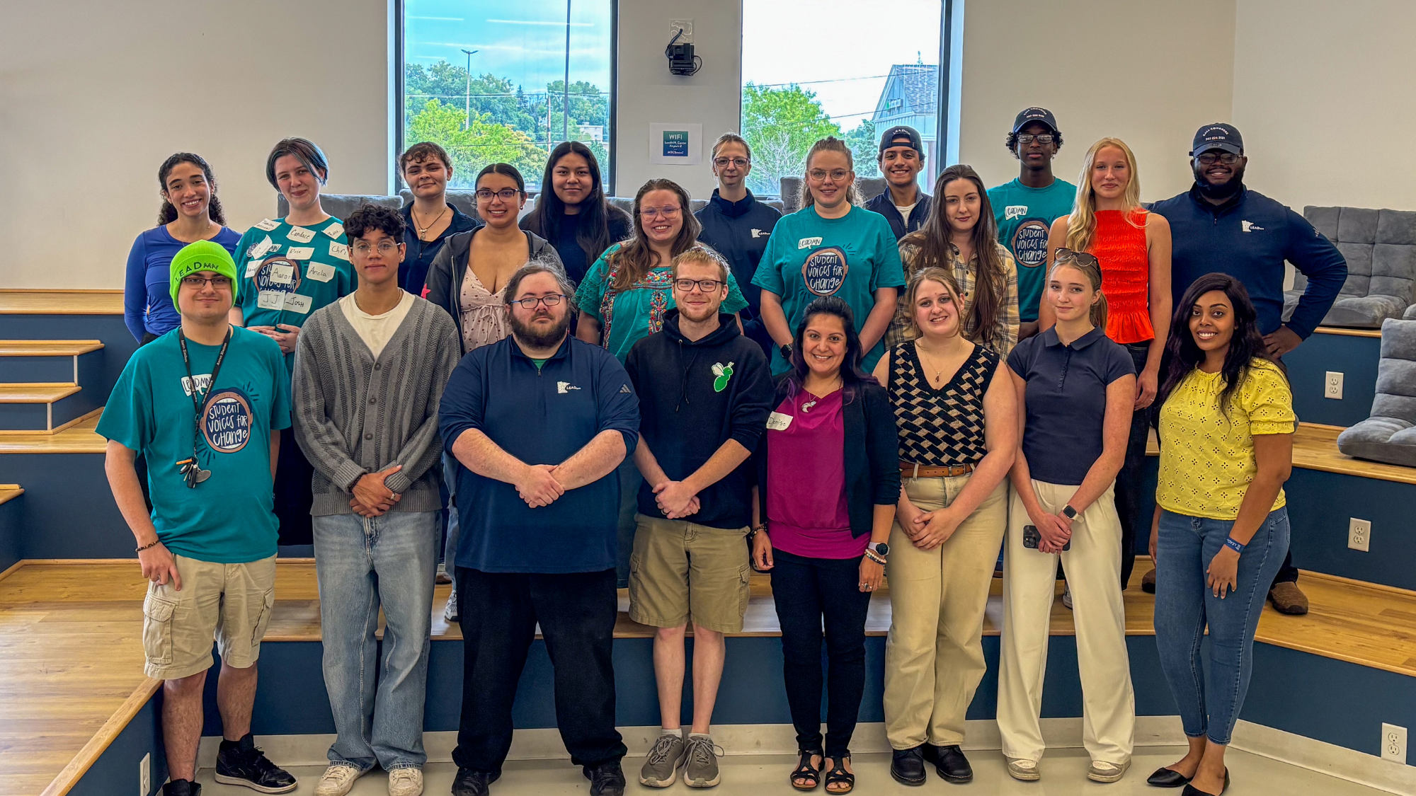 group photo of 20 students smiling in front of windows at the LeadMN office