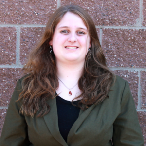 photo of olivia small, video production associate against red/copper brick