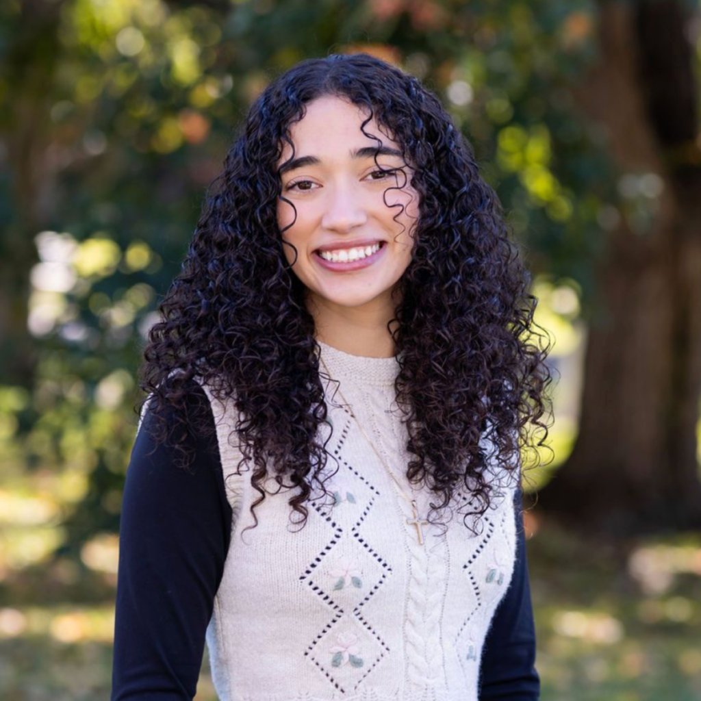 photo of lia alvarez, system advocate, standing in front of trees and greenery